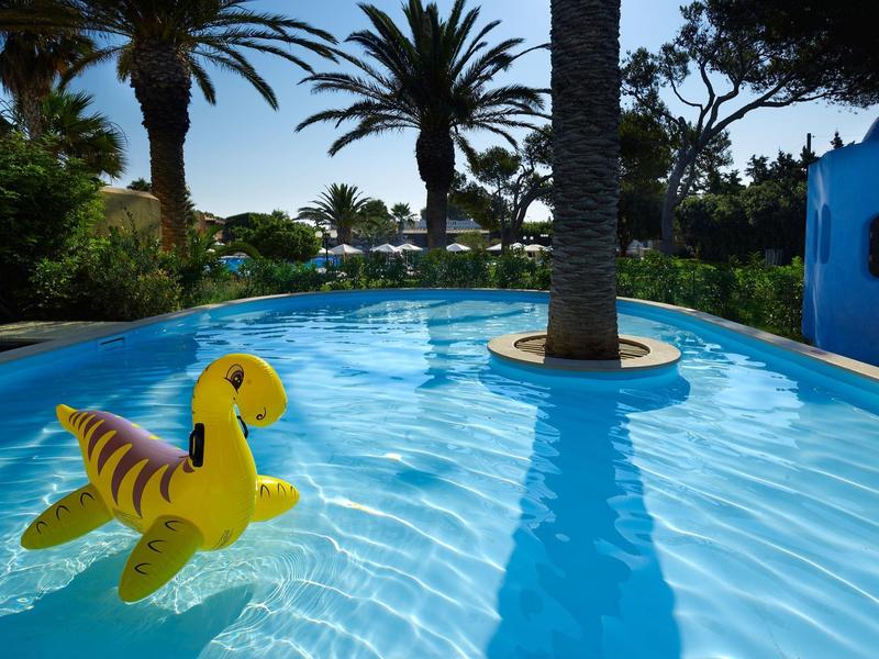 Pool mit Palmen und einem gelben aufblasbaren Spielzeug im Wasser bei Sonnenschein