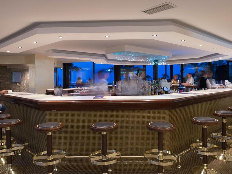 Eine moderne Hotelbar mit runden Hockern und Blick auf das Meer bei Dämmerung.