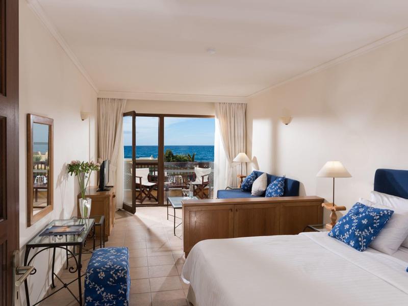 Helles Hotelzimmer mit Doppelbett, Balkon und Meerblick, modernes Dekor und gemütliche Sitzbereiche.