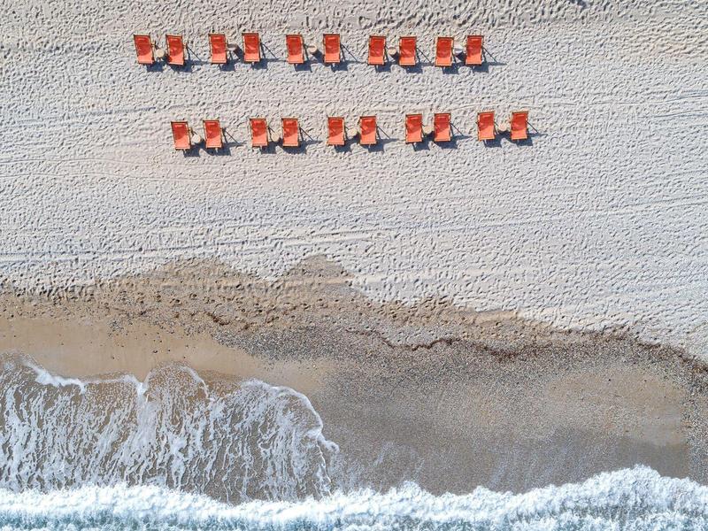 Sandstrand mit Reihen von orangenen Liegestühlen und welligem Meer im oberen Bereich.