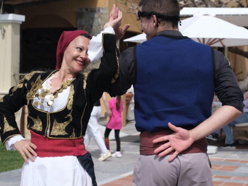 Paar in traditioneller Kleidung tanzt im Freien mit hellen Gebäuden im Hintergrund.