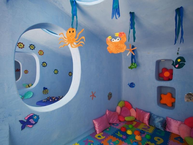 Buntes Kinderzimmer mit Meeresmotiven an den Wänden und Spielsachen auf dem Boden.