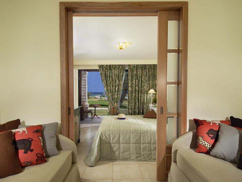 Blick in Schlafzimmer mit hellen Wänden, grünen Vorhängen und beige Sofa mit bunten Kissen.