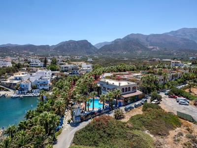 Veduta panoramica di una città costiera con hotel, piscina, acqua e montagne sullo sfondo.