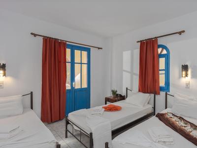 Camera accogliente con pareti bianche, porta blu, tende rosse e due letti singoli.