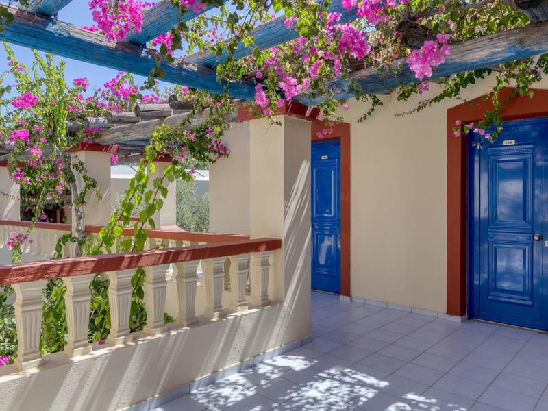 Balcone con piastrelle bianche, bougainville fiorite e porte blu in una giornata soleggiata.