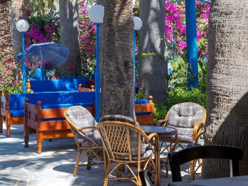 Area salotto all'aperto con sedie in rattan e tavolo di legno sotto palme in un giardino colorato