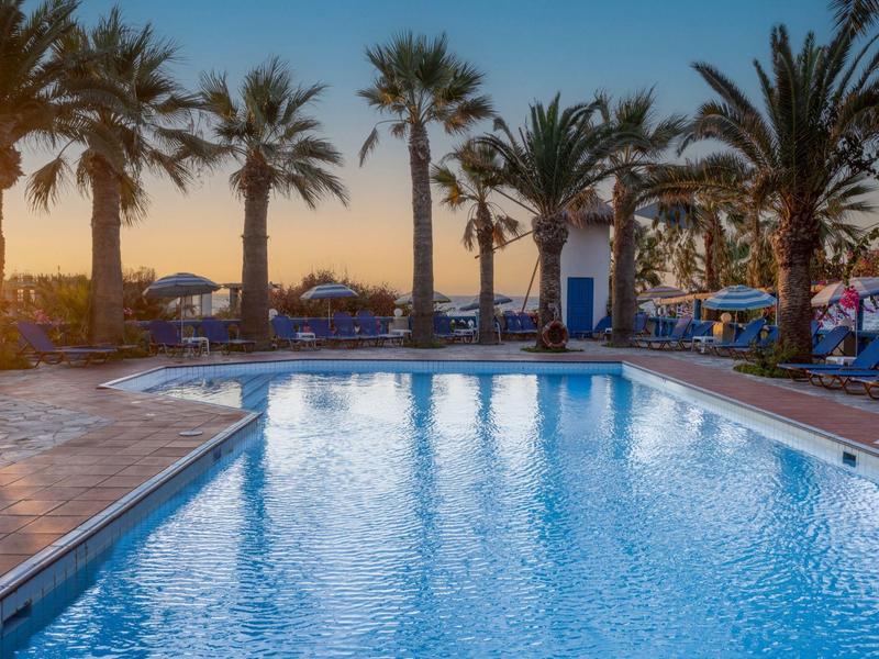 Piscina con lettini e palme al tramonto in un resort