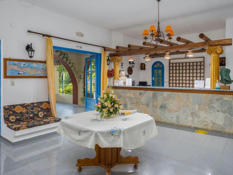 Bancone della reception luminoso con fronte in pietra, travi in legno e tavolo decorativo in stile mediterraneo.