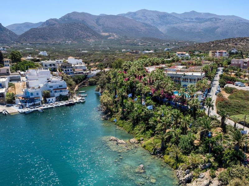 Vista di una città costiera con acqua limpida, palme verdi e montagne sullo sfondo.