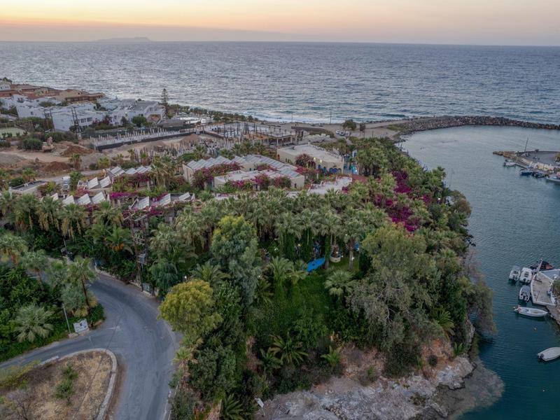 Veduta aerea di una città costiera con porto, mare e colline boschive al tramonto.