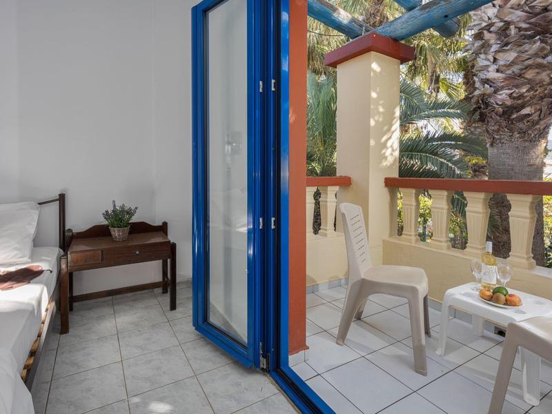 Balcone con sedie bianche e tavolo accanto a una stanza con finestra blu aperta.