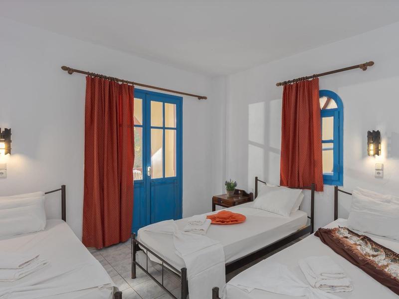 Camera accogliente con pareti bianche, porta blu, tende rosse e due letti singoli.