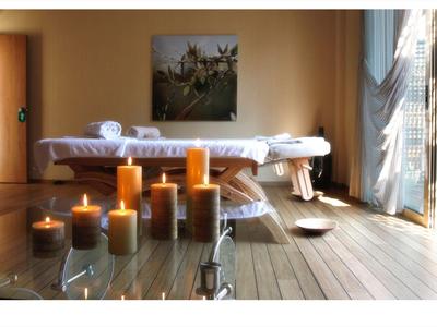 Světelná místnost s masážním stolem, zapálenými svíčkami a otevřenou záclonou.