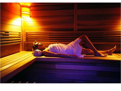 Osoba relaxující v sauně s teplým osvětlením a dřevěnými lavicemi.