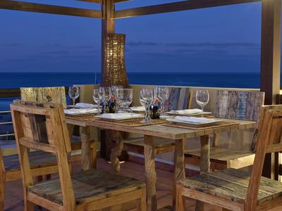 Rustikální dřevěný jídelní stůl se židlemi na balkoně s výhledem na moře za soumraku.