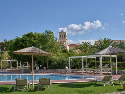 Pool mit Liegestühlen und Sonnenschirmen in einer grünen Gartenanlage unter blauem Himmel.