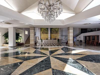Prostorná hotelová hala s geometrickou mramorovou podlahou a moderním lustrem.