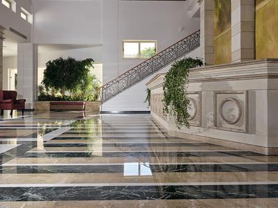 Elegantní hotelová hala s mramorovou podlahou, schodištěm a zelenými rostlinami.