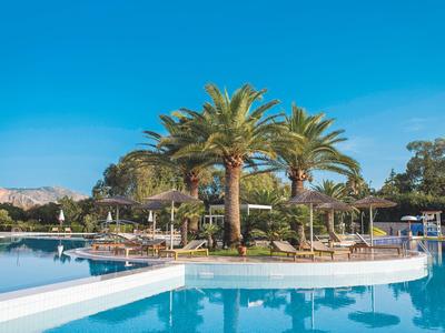 Riesiger Pool mit Palmen und Sonnenschirmen vor klarem blauem Himmel.