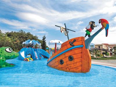 Světly hotelový pokoj s manželskou postelí, pohovkou, lampičkami a přístupem na balkon s výhledem.