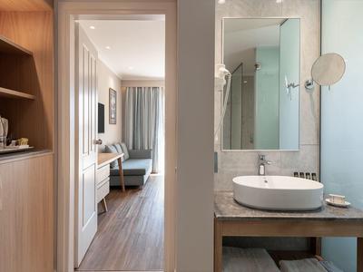 Moderní hotelová chodba s výhledem na obývací pokoj a koupelnu se umyvadlem.