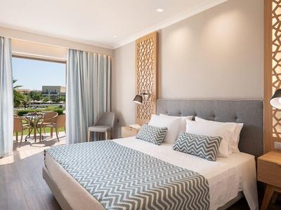 Světý hotelový pokoj s velkou postelí, moderním zařízením a přístupem na terasu s výhledem na zahradu.