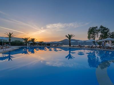 Großer Pool mit Palmen und Sonnenuntergang am Horizont in einem Hotelresort.