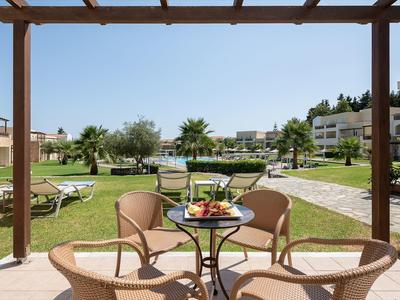 Terasa se stolkem, židlemi a talířem s jídlem s výhledem na zahradu a bazén v hotelu.