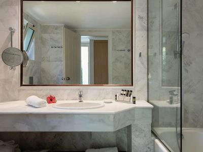Moderní hotelová koupelna s mramorovým umyvadlem, velkým zrcadlem, skleněným sprchovým koutem a uspořádanými doplňky.