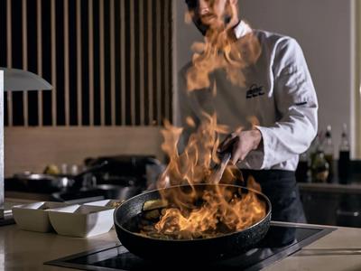 Šéfkuchař vaří s plameny stoupajícími z pánve v moderní kuchyni.