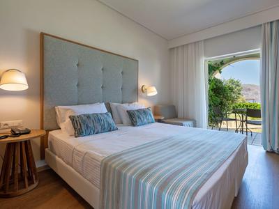 Světlná ložnice s manželskou postelí, nočními stolky a výhledem do zahrady přes otevřené dveře.