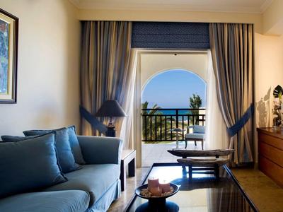 Pohodlný hotelový pokoj s pohovkou, závěsy a balkonem s výhledem na moře.