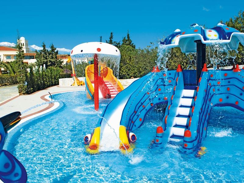 Barevné vodní hřiště se skluzavkami v bazénu za slunečného dne.