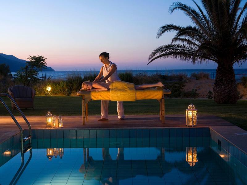 Žena si užívá masáž u bazénu při západu slunce v tropickém lázeňském prostředí.