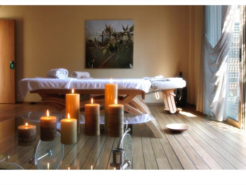 Světelná místnost s masážním stolem, zapálenými svíčkami a otevřenou záclonou.