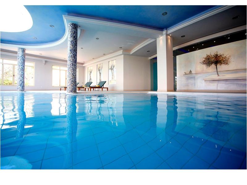 Vnitřní bazén s modrými dlaždicemi a moderním, světlým zařízením.