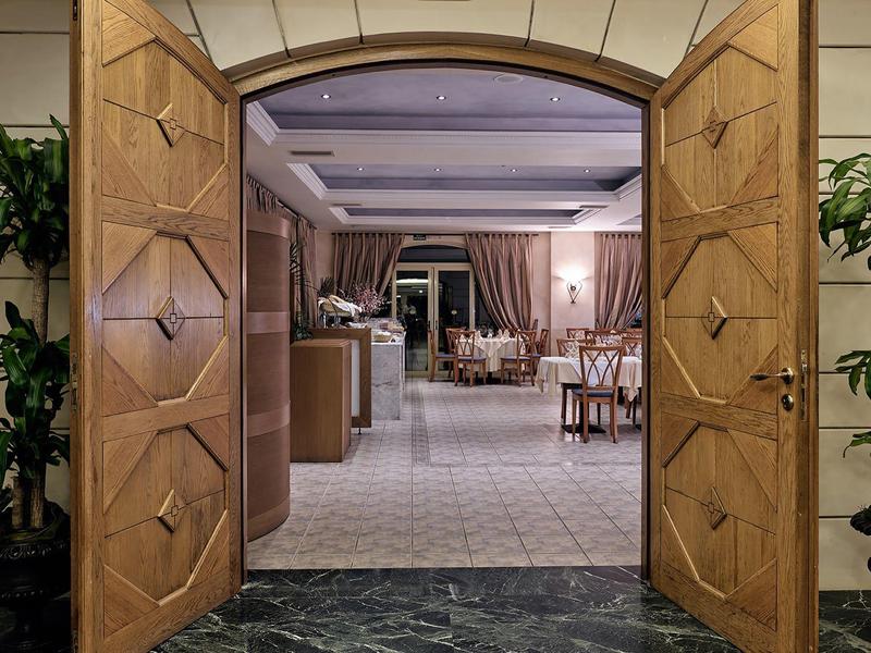 Otevřené dřevěné dveře vedou do elegantní jídelny se stoly a židlemi.