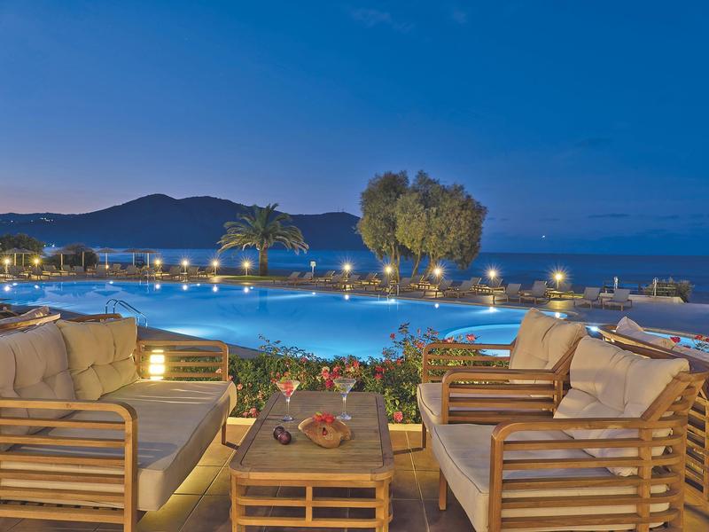 Pohodlná sezení u osvětleného bazénu s výhledem na moře za soumraku.