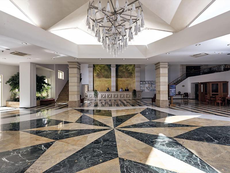 Prostorná hotelová hala s geometrickou mramorovou podlahou a moderním lustrem.