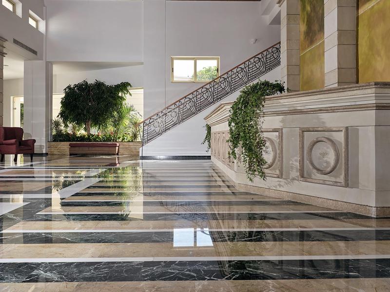 Elegantní hotelová hala s mramorovou podlahou, schodištěm a zelenými rostlinami.
