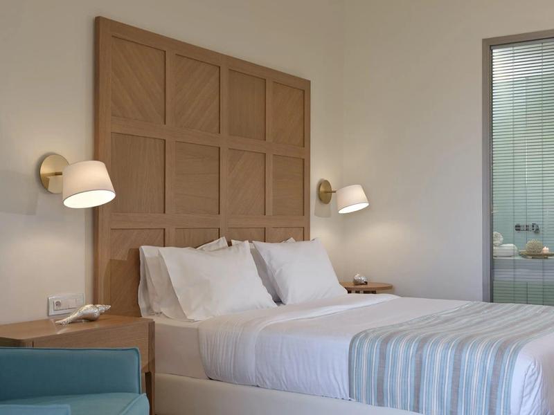 Hotelový pokoj s upravenou postelí, dřevěným čelem postele, nástěnnými lampami a nočními stolky.