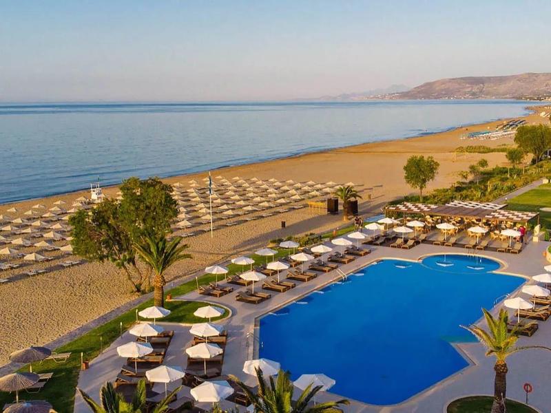 Pohled na velký bazén s lehátky na písečné pláži s výhledem na moře.