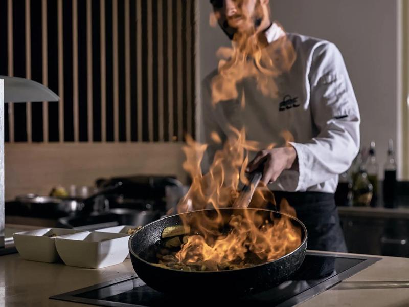 Šéfkuchař vaří s plameny stoupajícími z pánve v moderní kuchyni.
