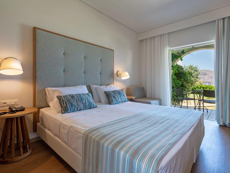 Světlná ložnice s manželskou postelí, nočními stolky a výhledem do zahrady přes otevřené dveře.