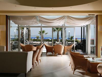 Salon lumineux avec fauteuils et vue sur terrasse, mer et palmiers.