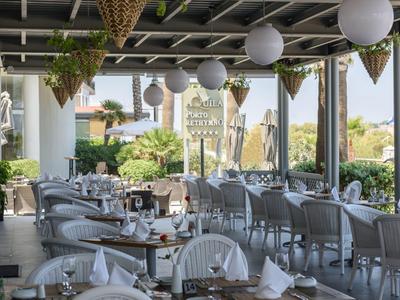 Terrasse couverte avec chaises, tables dressées et pots de plantes suspendus.