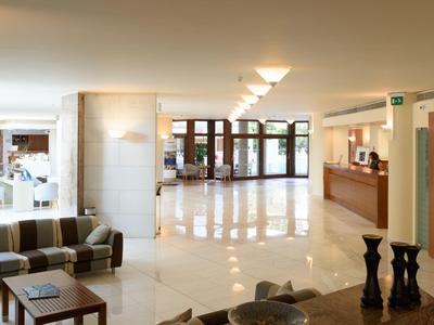 Hall d'hôtel lumineux avec réception, coin salon et sol en marbre brillant.