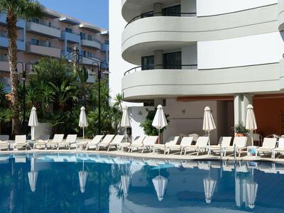 Complexe hôtelier moderne avec piscine, transats et parasols devant la façade.