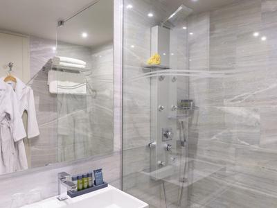 Salle de bain moderne avec douche en verre, peignoirs blancs et serviettes accrochées au mur.